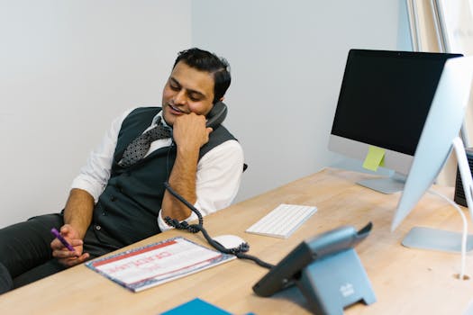 Smiling businessman engaged in a phone conversation at a modern office desk.